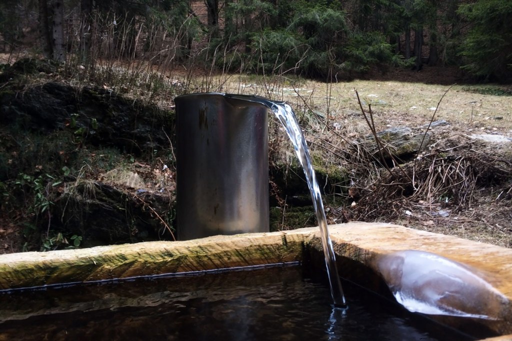 l'acqua che fuoriesce da un ugello in acciaio lucido si riversa in una vasca di legno perfettamente intagliata