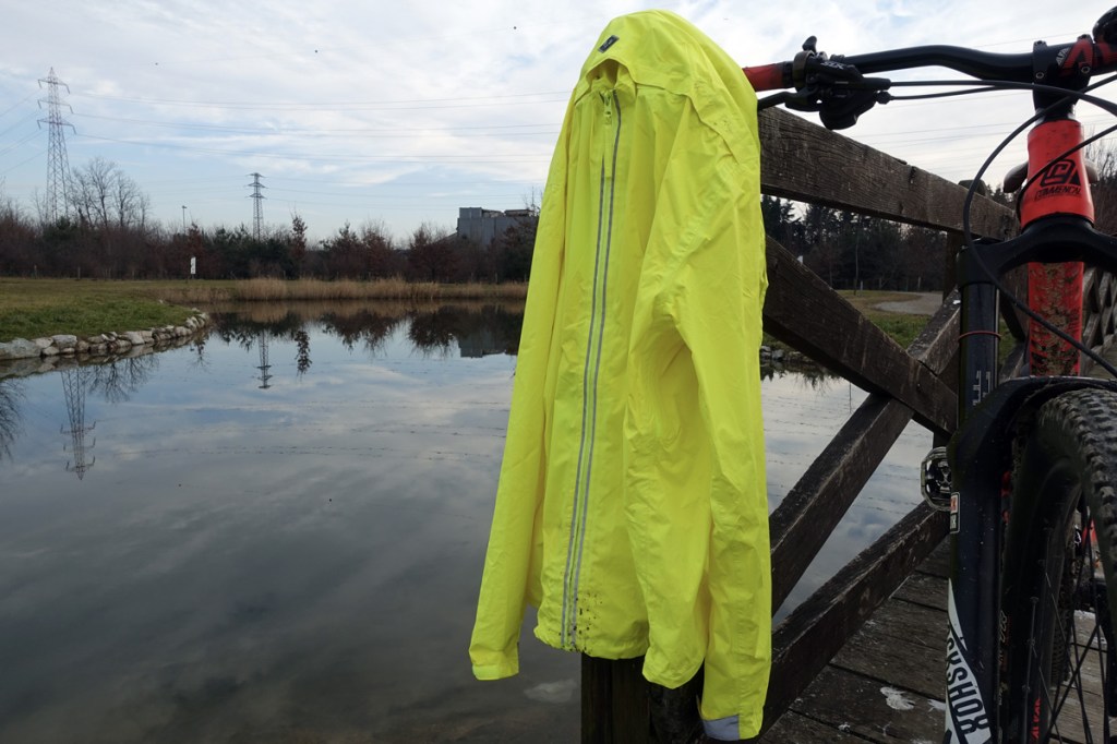 in foto una giacca antipioggia gialla fluorescente con sullo sfondo un laghetto artificiale