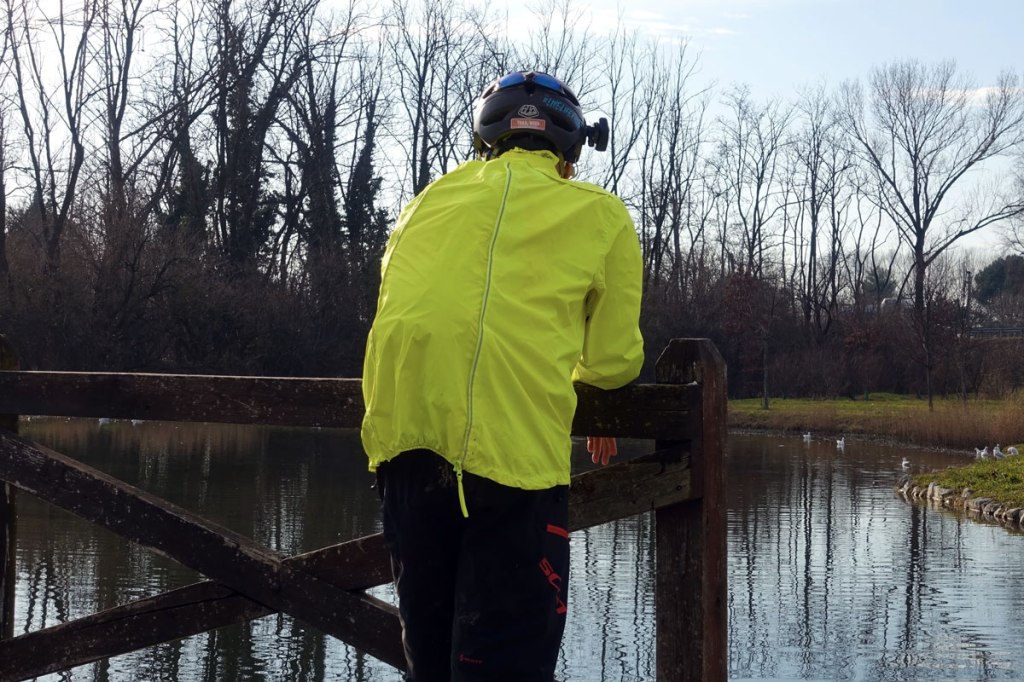 in foto un ciclista indossa una giacca antipioggia nei pressi di un laghetto artificiale