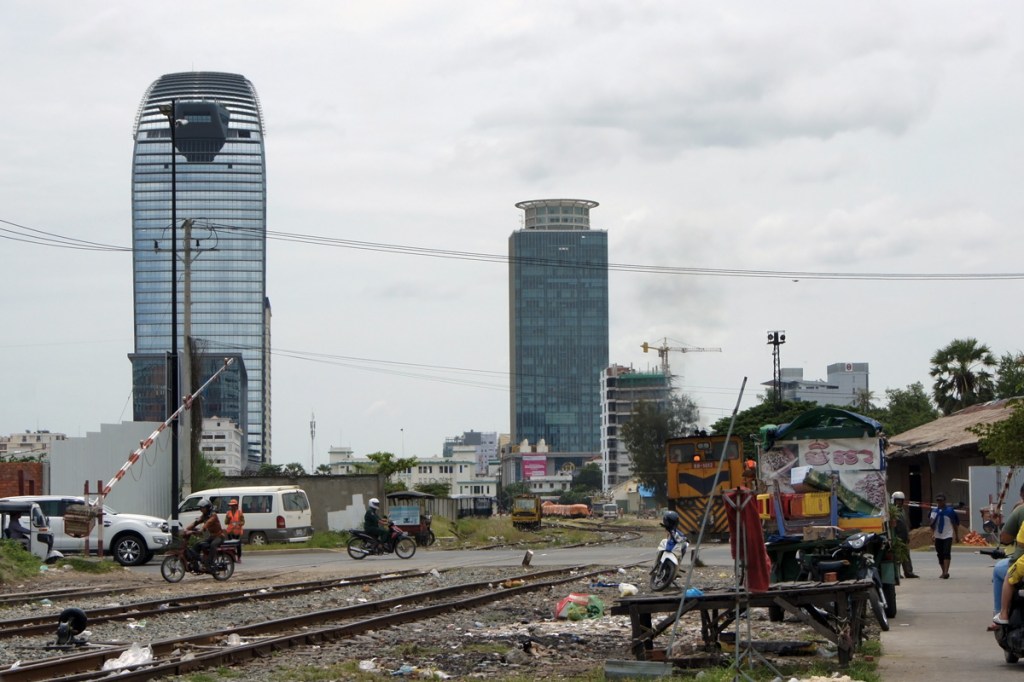nella foto baracche a phnom phen, lavoratori che si spostano in moto, il grattacelo coreano ed il grattacielo cinese vicino i binari del treno