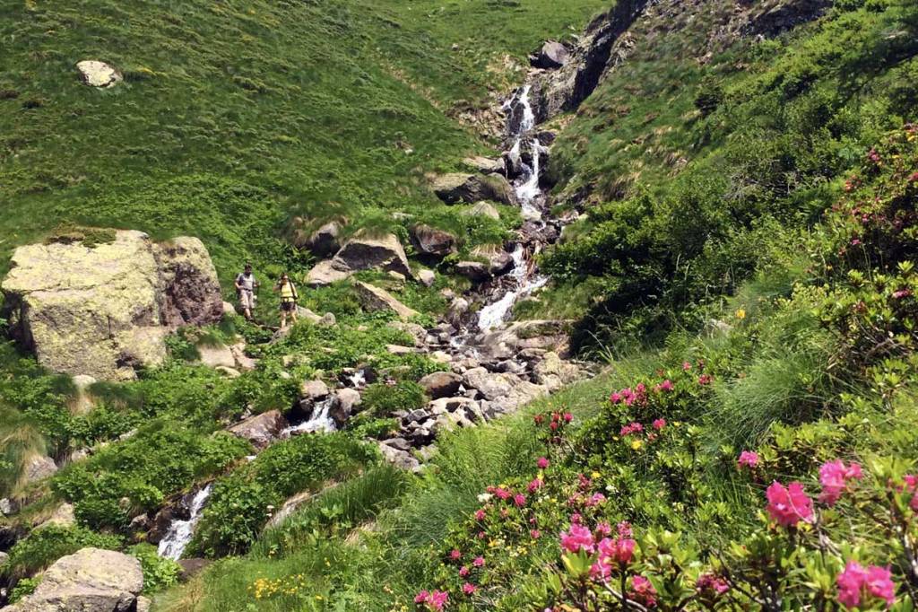 in foto due escursionisti in discesa approcciano un ruscello che attraversa un sentiero nelle orobie bergamasche