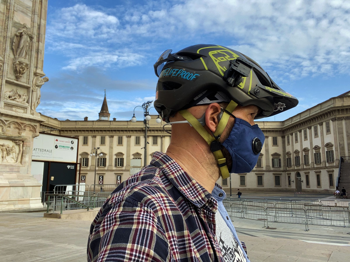un rider milanese con casco, mascherina e cuffie a conduzione ossea nella piazza del Duomo