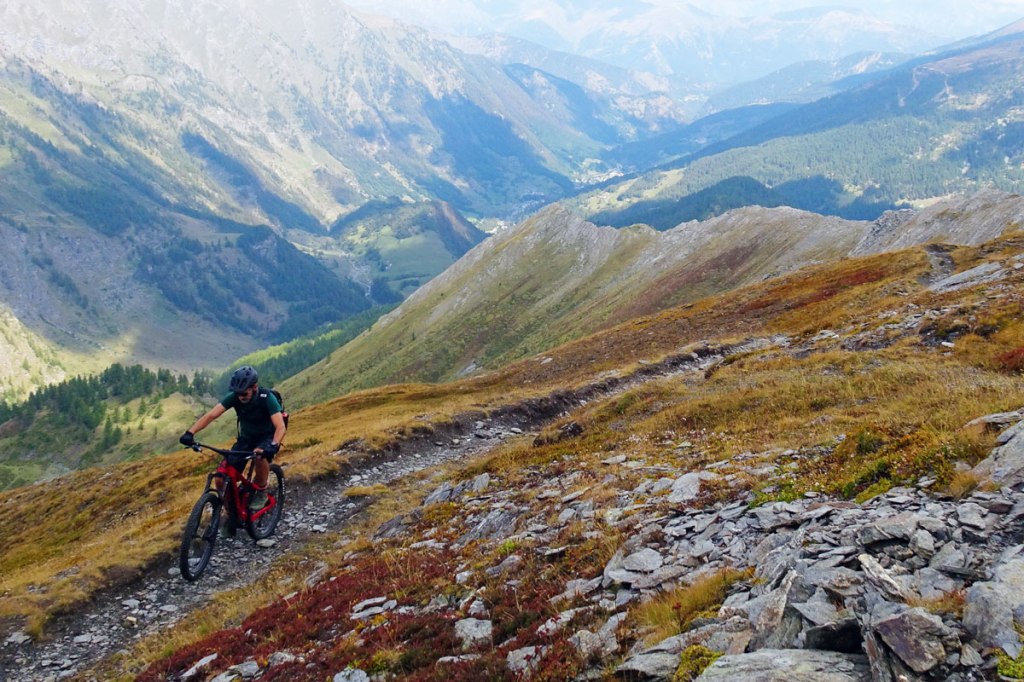 un biker in mountain bike in salita lungo un sentiero che si affaccia su una valle panoramica