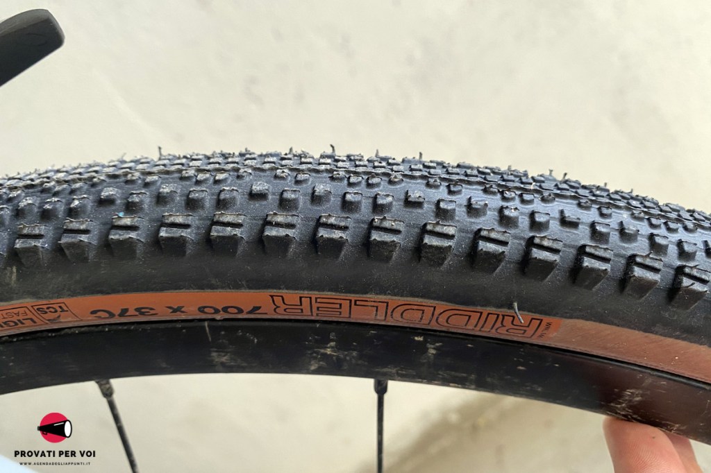 primo piano del battistrada di uno pneumatico per bicicletta gravel bike e sullo sfondo una strada in calcestre e foglie secche