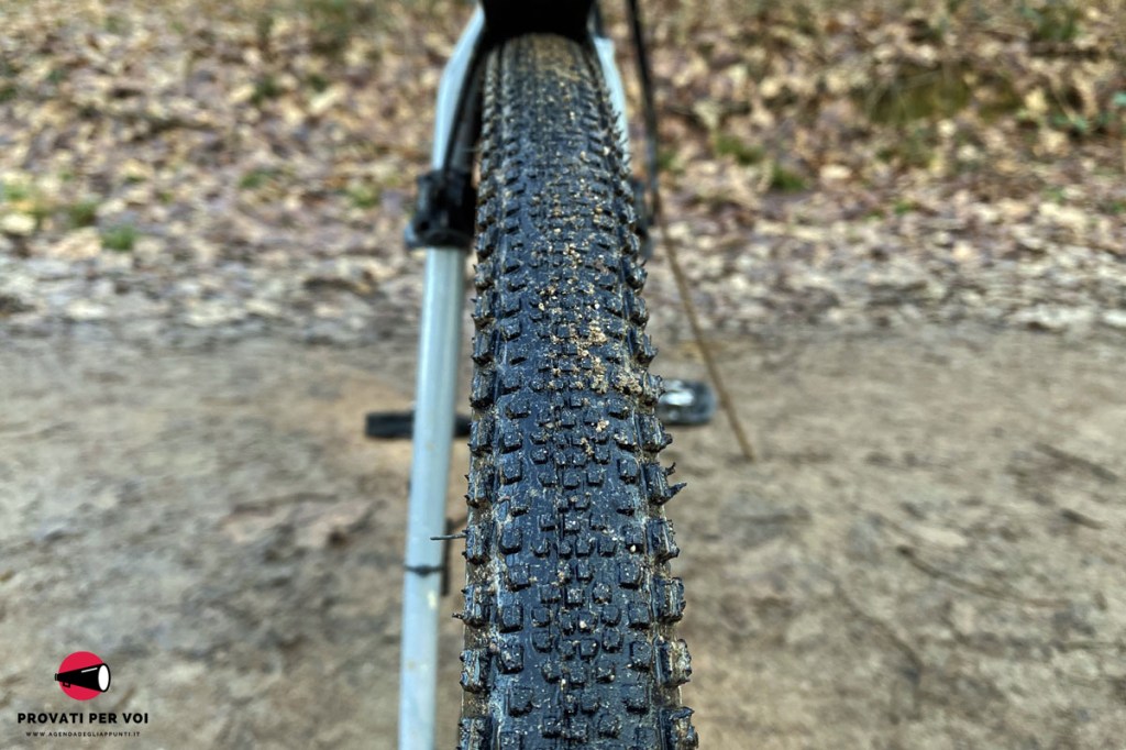 primo piano del battistrada di uno pneumatico per bicicletta gravel bike e sullo sfondo una strada in calcestre e foglie secche