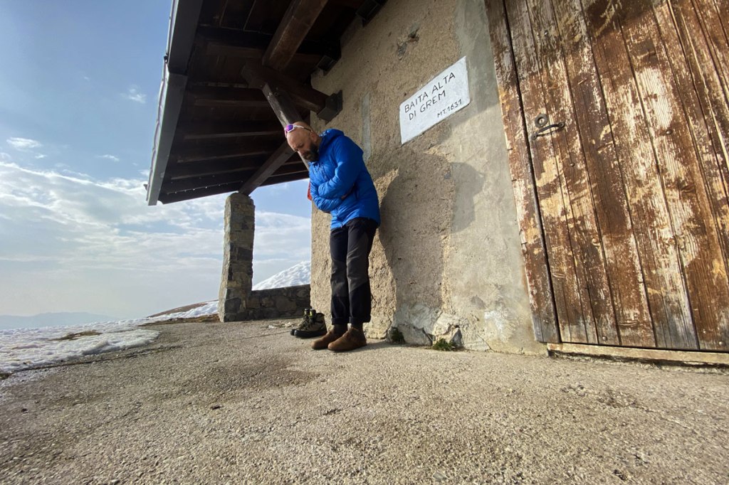 un ragazzo appoggiato al muro di una baita circondata dalla neve