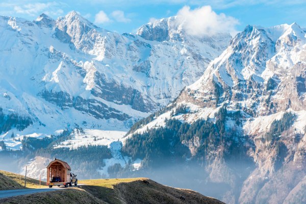 un'autovettura con casa su carrello appendice e sullo sfondo un gruppo di montagne innevate