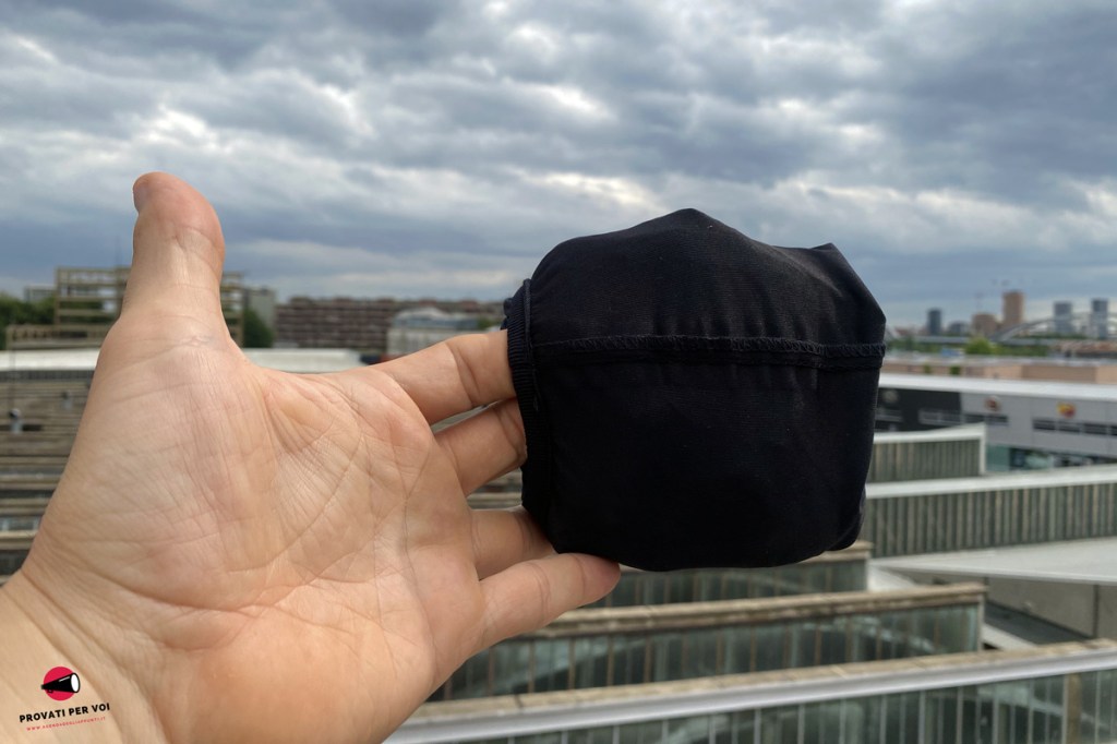 una giacca raggomitolata su se stessa e tenuta da due dita della mano per metterne in evidenza le dimensioni ridotte
