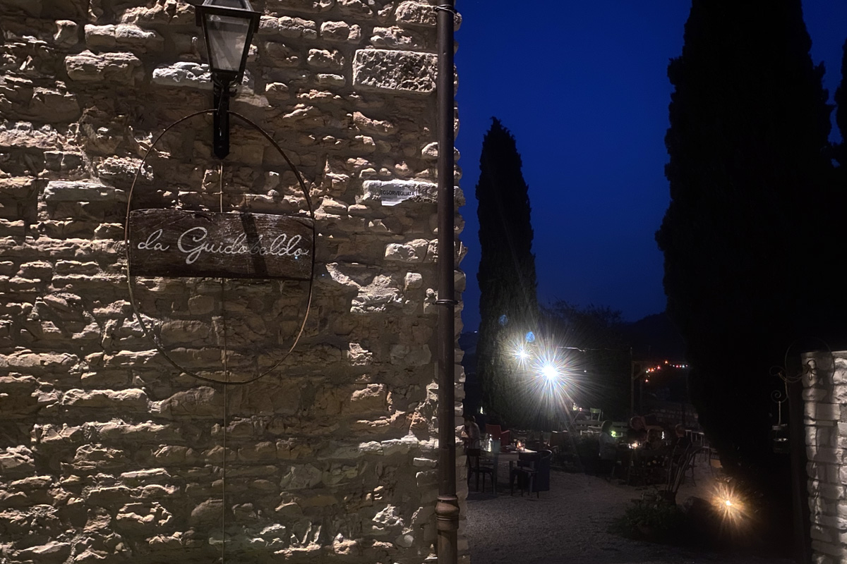 il giardino di un ristorante illuminato di notte ed in primo piano l'insegna su muro di pietra