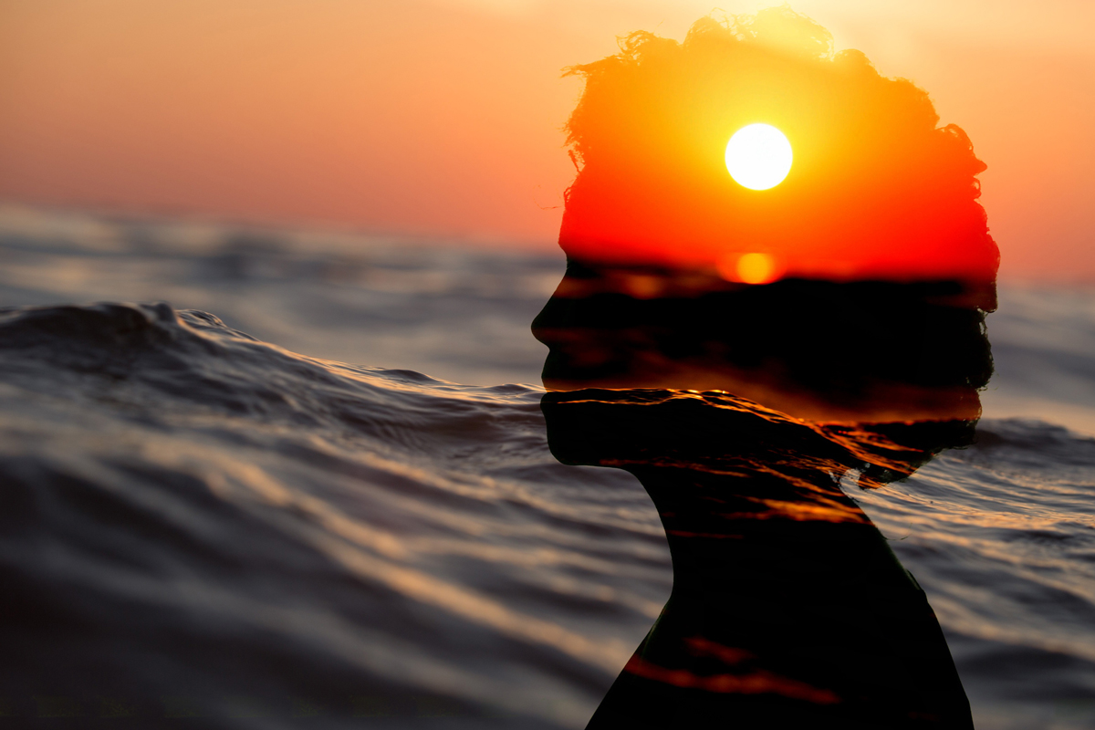 un viso di donna di profilo con acqua di mare e sole al tramonto sullo sfondo