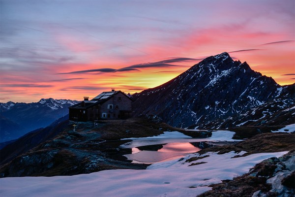 Un rifugio di montagna sulle Alpi vicino ad un laghetto parzialmente coperto dalla neve