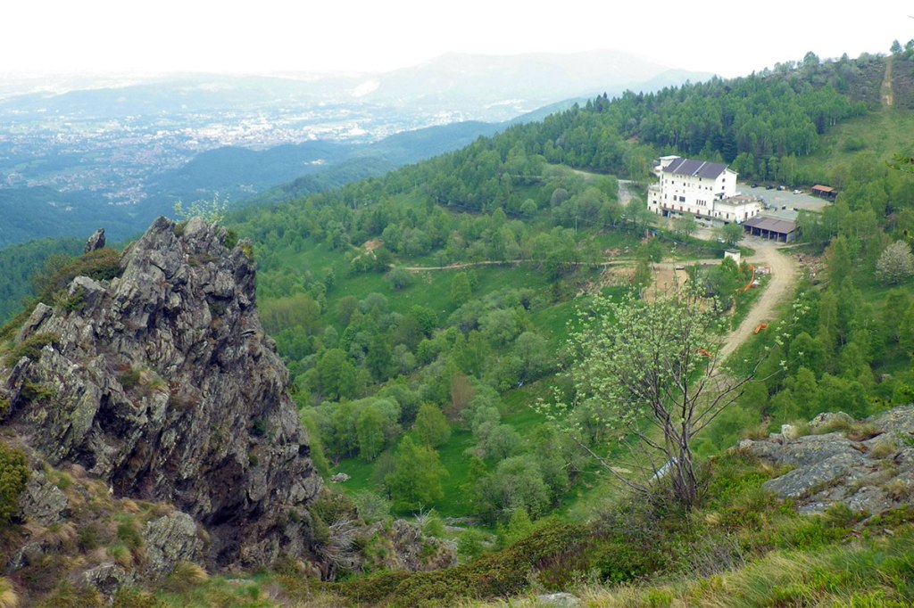 uno sperone di roccia in primo piano, il rifugio aquila di giaveno in secondo pinao e sullo sfondo la pianura