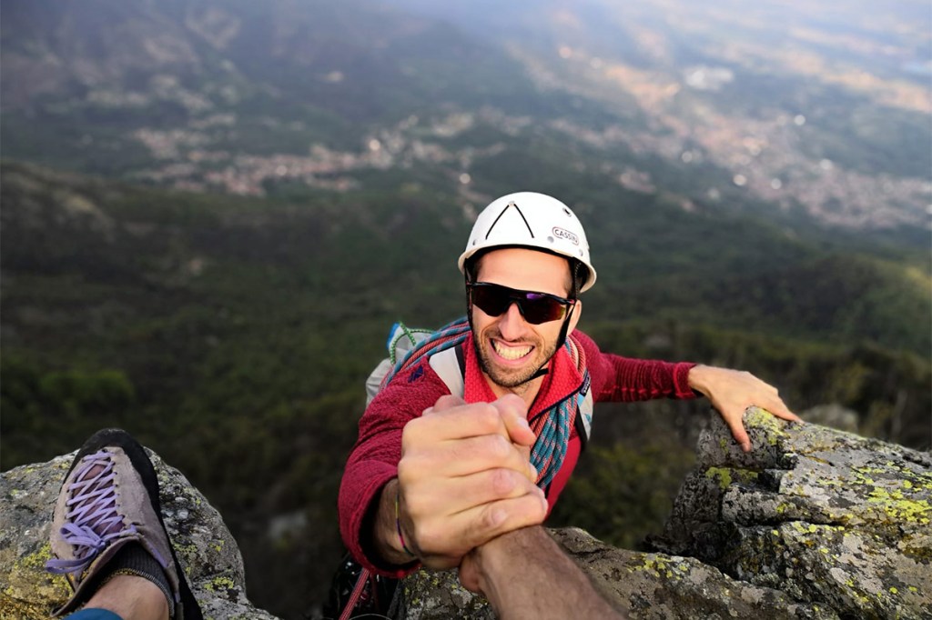 un alpinista stringe la mano che gli porge un suo amico all'arrivo in vetta