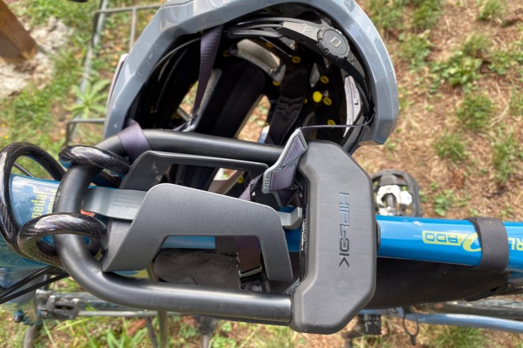 in primo piano un lucchetto di sicurezza per biciclette del tipo U lock di colore nero assicura una bicicletta di colore blu ad rastrelliera