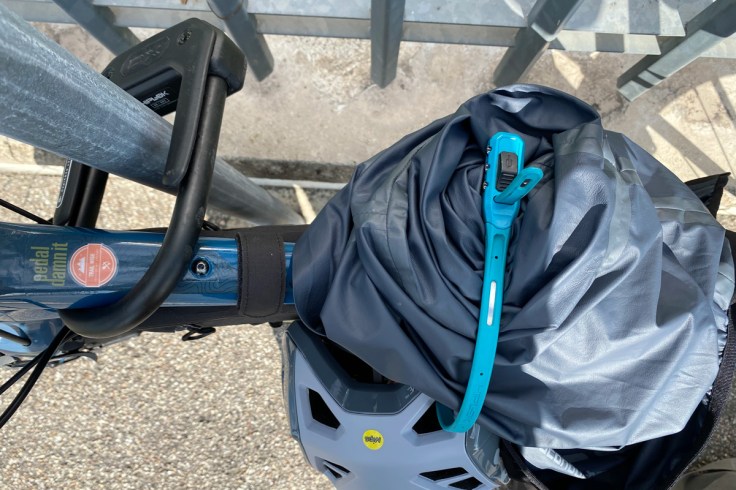una bicicletta assicurata ad un palo con un lucchetto della serie U Lock una giacca tecnica ed un casco legati insieme alla bicicletta grazie ad un lucchetto a fascetta di nuova generazione