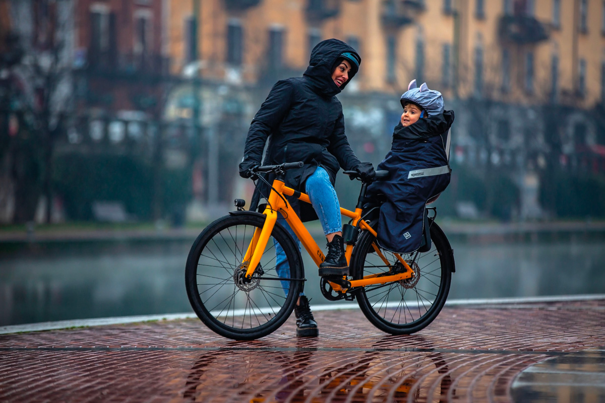 una signora in bici sotto la pioggia insieme alla sua bambina protette da capi di abbigliamento idrorepellenti