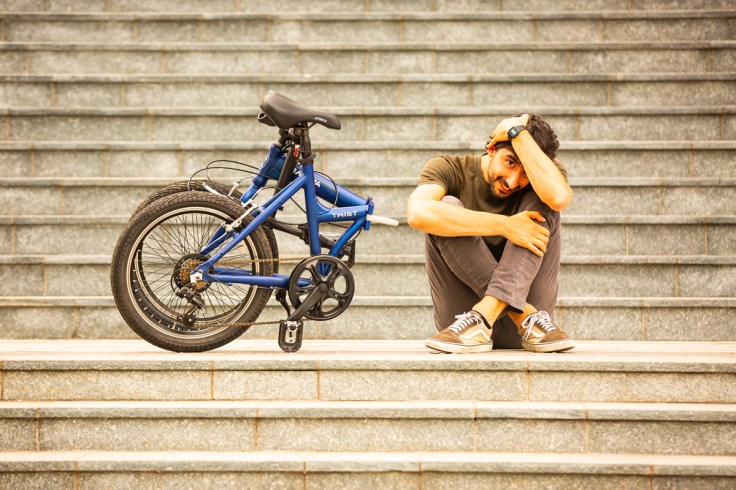 un ragazzo insieme alla sua bici pieghevole trova un momento di svago seduto su una scalinata