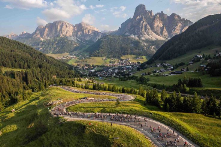 un gruppo di ciclisti si snoda su una strada di montagna durante una manifestazione con sullo sfondo le magnifiche Dolomiti