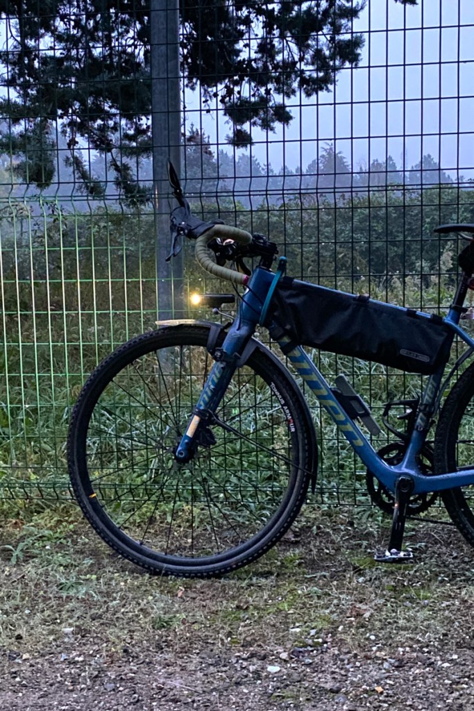 una bicicletta gravel bike è appoggiata alla rete di protezione che separa una pista ciclabile in ghiaia dal campo pratica del golf club Idea Verde