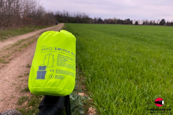 un gilet reversibile ad alta visibilità conforme al codice della strada arrotolato e riposto all'interno della sua custodia di trasporto sullo sfondo un campo coltivato e una strada campestre