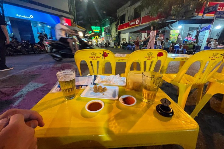 un tavolino giallo apparecchiato e delle sedie gialle in primo piano rubano quasi la scena ad una vivace strada di Hanoi, capitale del Vietnam