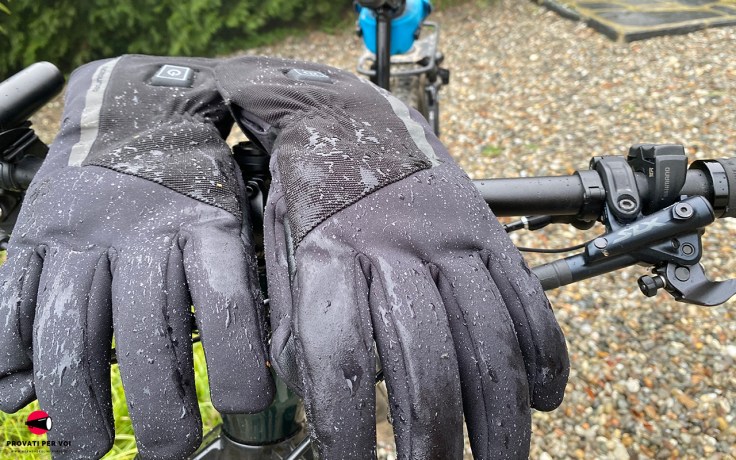 Guanti riscaldati Tucano Urbano Starwarm Hydroscud sotto la pioggia battente, appoggiati sul manubrio di una bicicletta