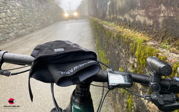Guanto riscaldato Tucano Urbano Starwarm Hydroscud sul manubrio di una bici in una giornata fredda e piovosa, con un’auto in arrivo sullo sfondo