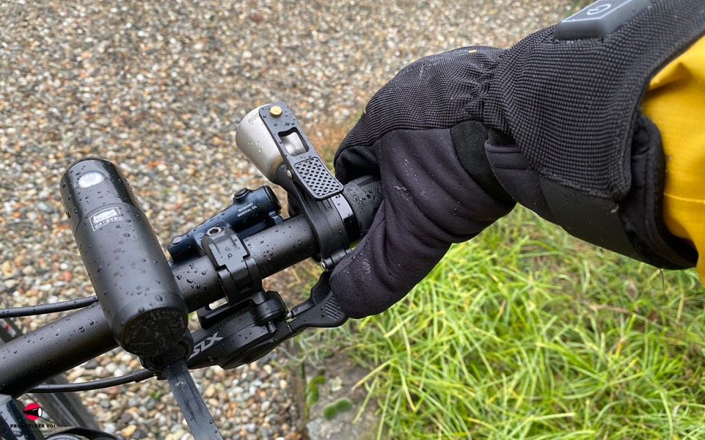 Il pollice di una mano che calza un guanto invernale mostra la presa con il dito sui comandi del cambio di una bicicletta mountain bike a pedalata assistita