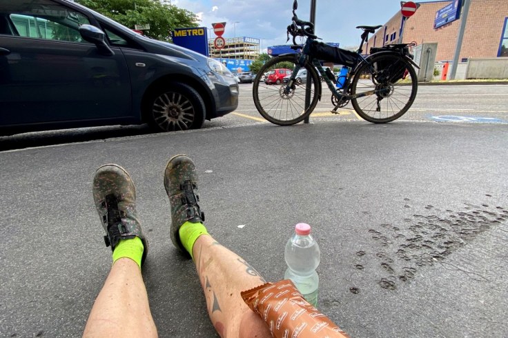 Ciclista in pausa dopo una pedalata con gelato sulla gamba accanto alla propria bicicletta parcheggiata.